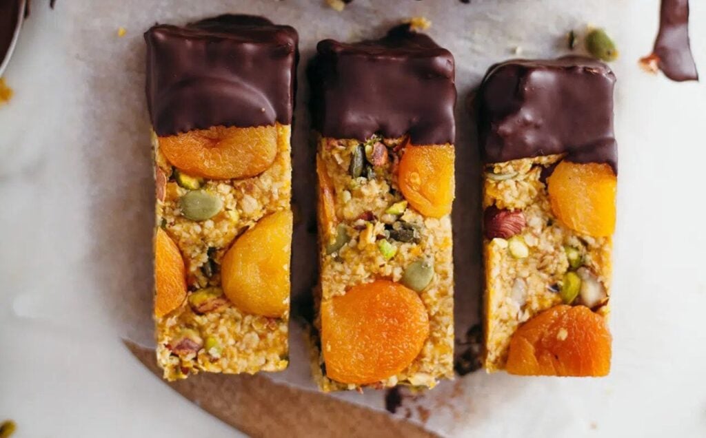Three raw vegan apricot energy bars dipped in chocolate, on a white marble surface