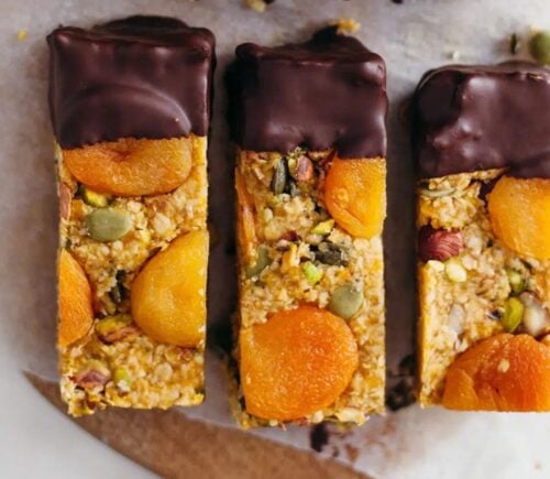Three raw vegan apricot energy bars dipped in chocolate, on a white marble surface