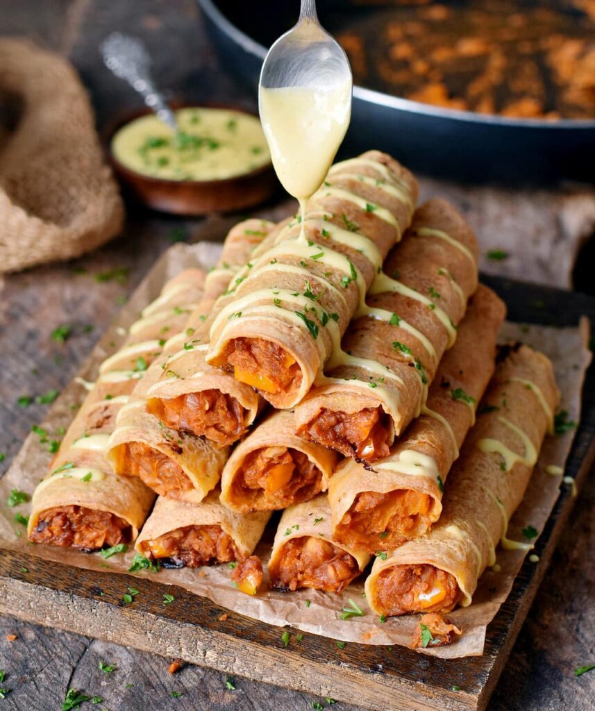 Vegan buffalo-flavored taquitos stacked on a wooden serving platter