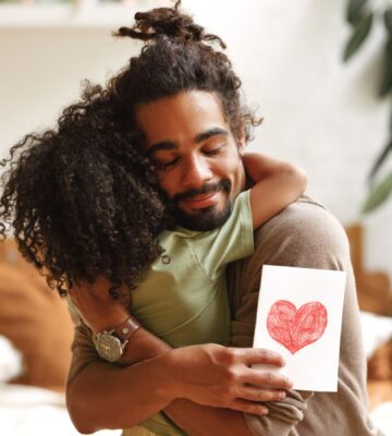 A man hugging his child holding a card with a heart on it on Father's Day