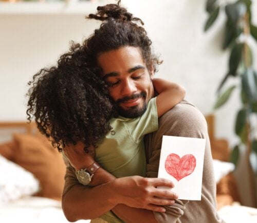 A man hugging his child holding a card with a heart on it on Father's Day