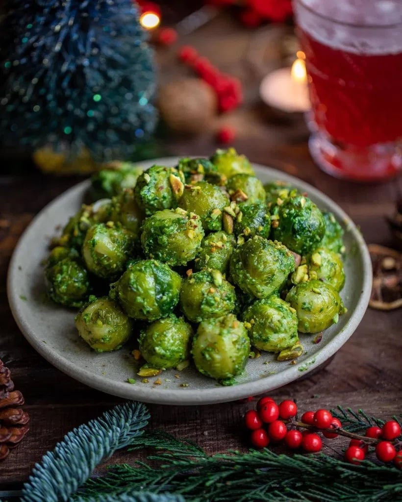 Photo shows a plate piled high with pesto brussel sprouts surrounded by festive decorations such as pine cones and red berries