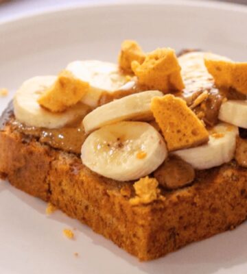 A slice of vegan banana bread topped with plant-based honeycomb, nuts, and slices of banana