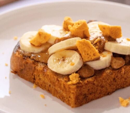 A slice of vegan banana bread topped with plant-based honeycomb, nuts, and slices of banana