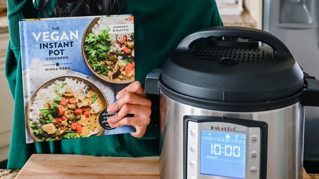 Hand holds a recipe book next to an Instant Pot multicooker