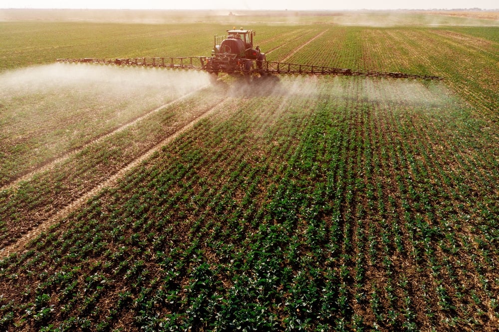 Tractor spraying pesticides over crops on a farm