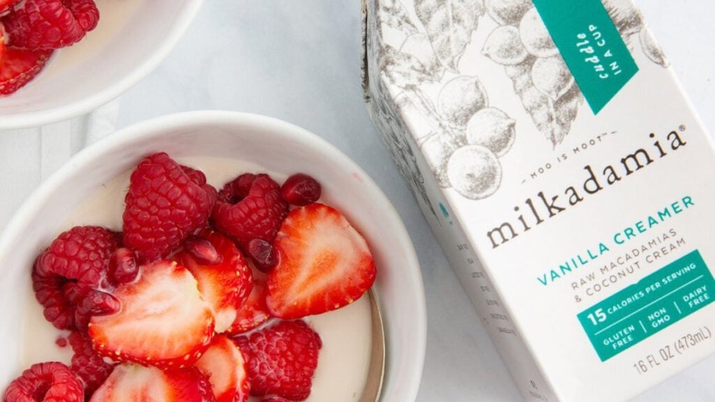 Vegan creamer containing coconuts made by Milkadamia beside a bowl of strawberries