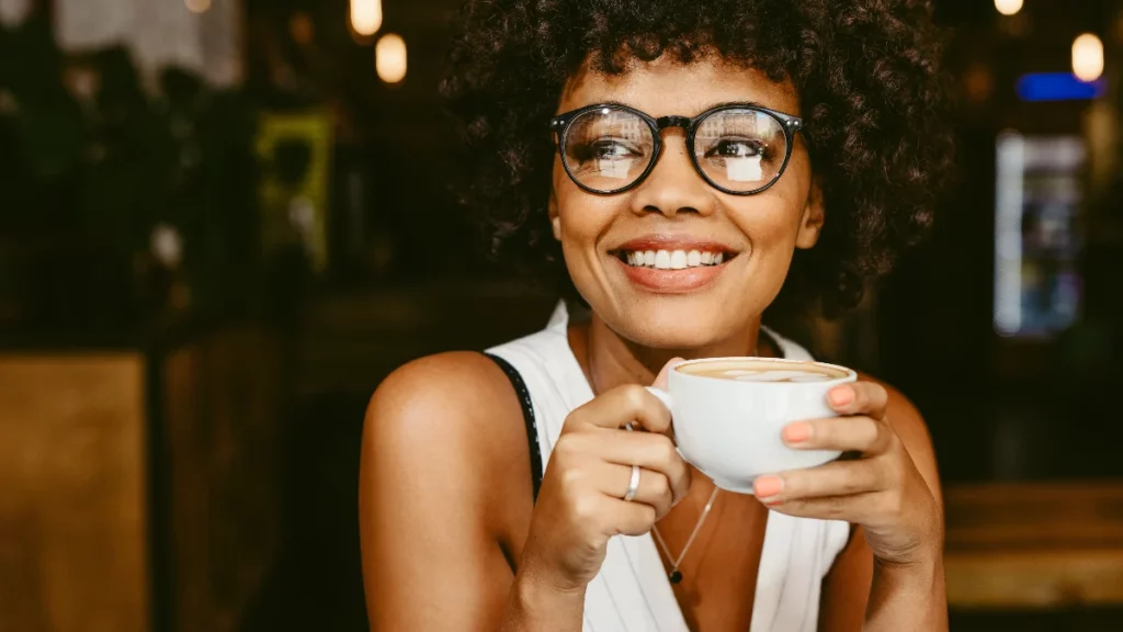 A woman wearing glasses drinking a coffee with non-dairy creamer