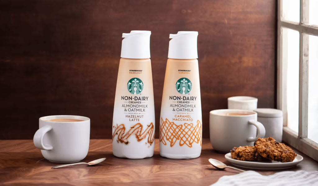 Vegan-friendly non-dairy coffee creamer in flavors caramel and hazelnut made by Starbucks, beside some mugs of coffee and some cookies