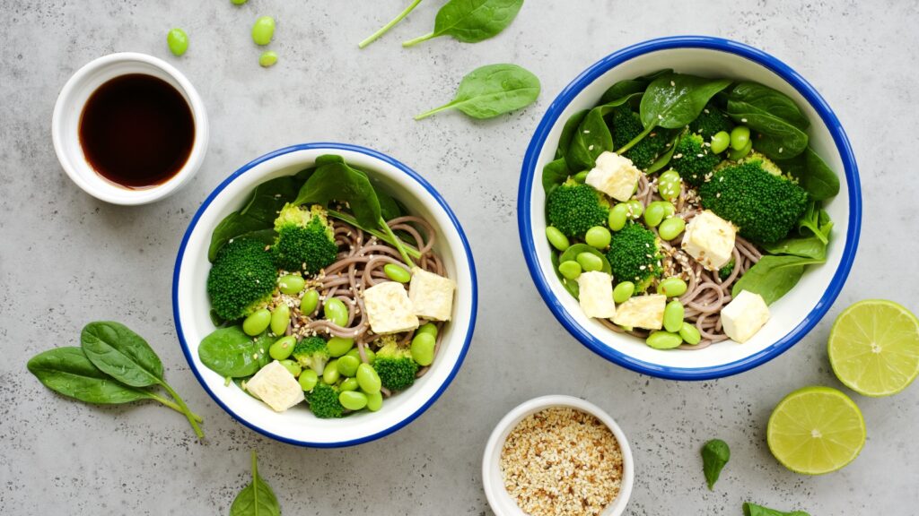 Two bowls of salad containing plant-based proteins, including edamame beans, tofu, and broccoli 