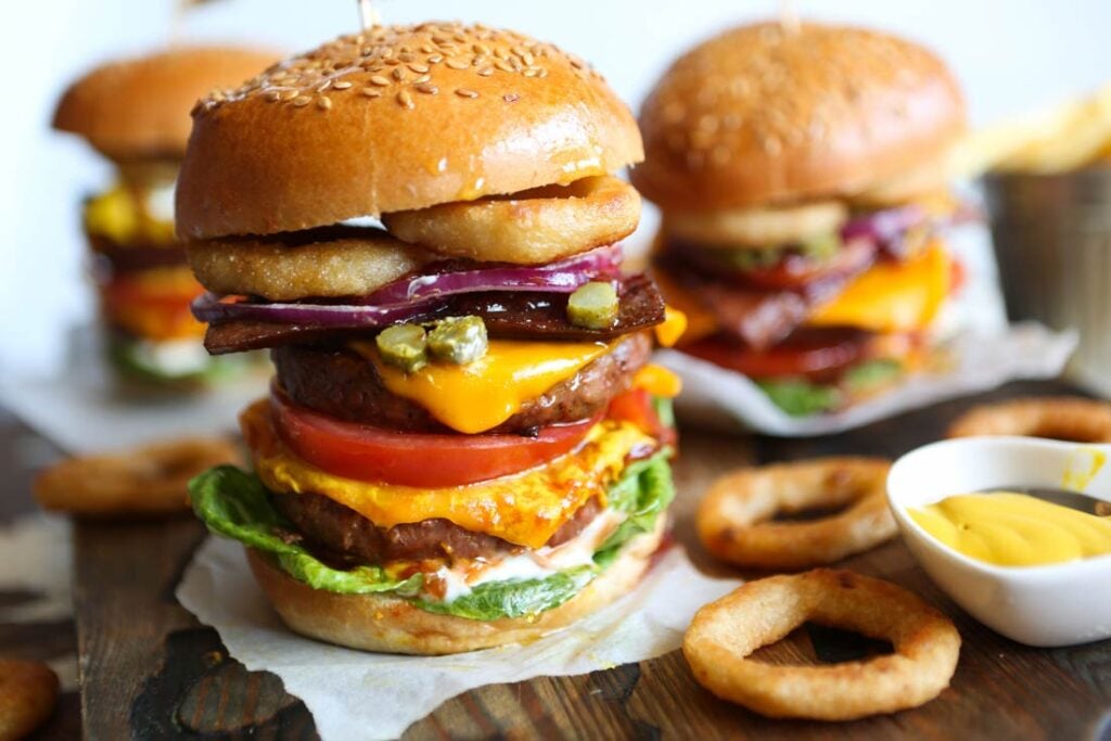 A vegan burger featuring onion rings, dairy-free cheese, plant-based patties, and salad