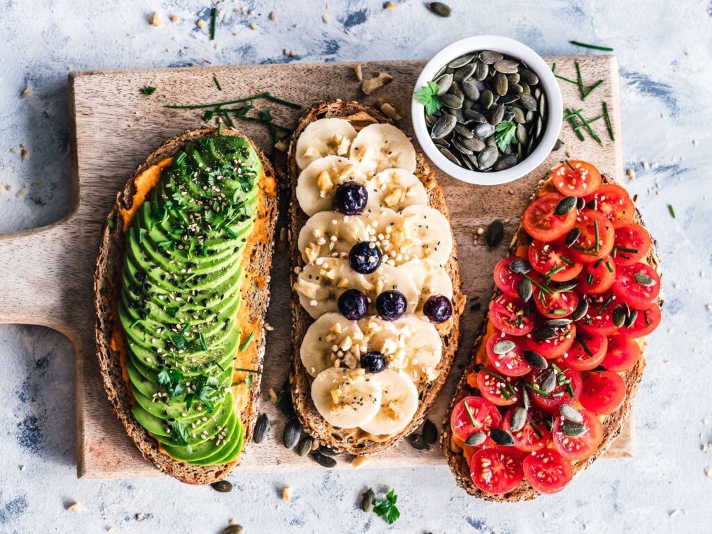 plant-based foods including avocado, banana, and cherry tomatoes on slices of bread