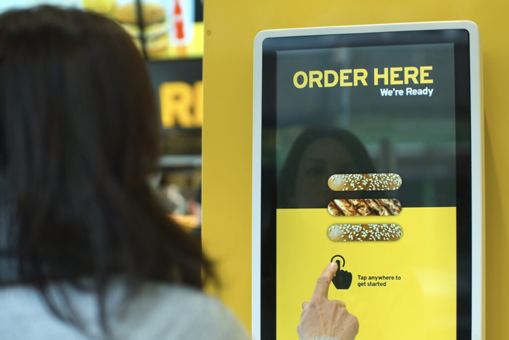 Person ordering fast food from a large wall-mounted touchscreen