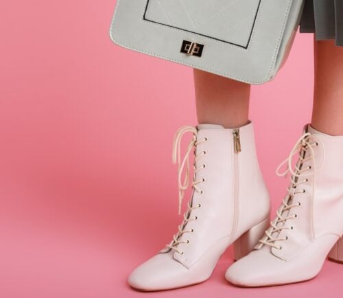 model wearing trendy white lace up ankle boots, holding stylish small green mint color faux leather bag, posing on pink background