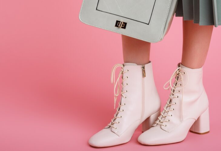 model wearing trendy white lace up ankle boots, holding stylish small green mint color faux leather bag, posing on pink background