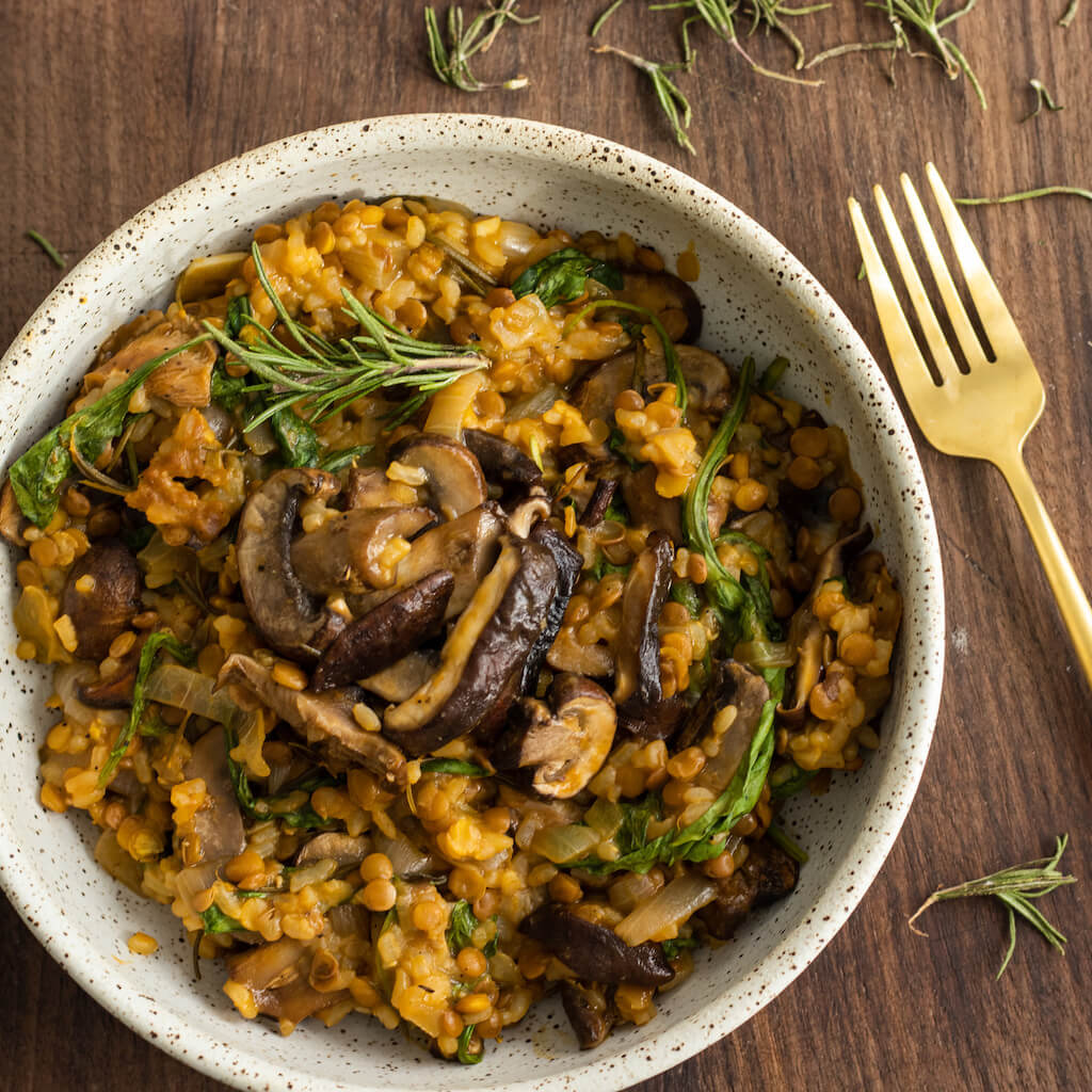 Vegan lentil mushroom risotto in a white stoneware bowl with a gold-tone fork placed beside it and stood on a wooden table