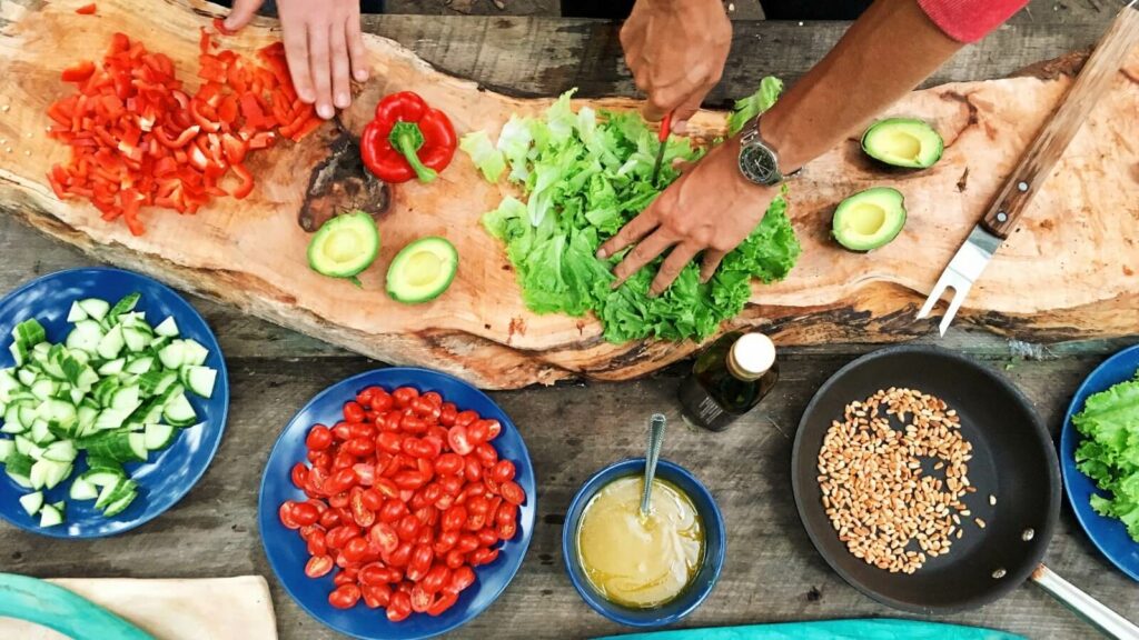 People chopping a variety of vegetables on a wooden table