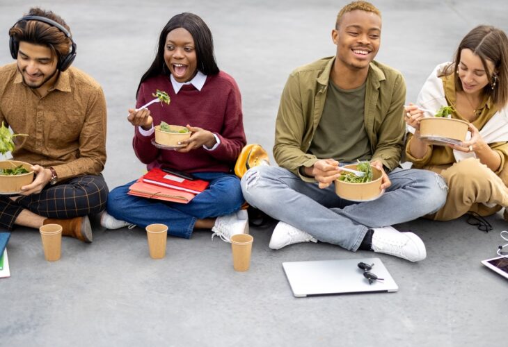 Students sit on the ground eating salad with their text books