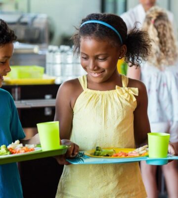 Children at school carrying trays of healthy food and smiling