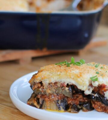 A square portion of Greek moussaka made to a vegan recipe, presented on a white circular plate with a silver fork