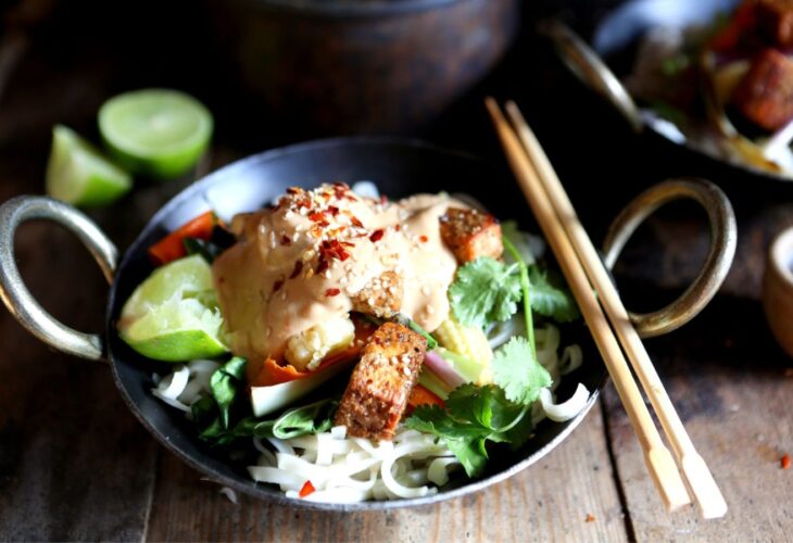 A wok filled with a vegan starry, topped with peanut satay sauce, with chopsticks to the side