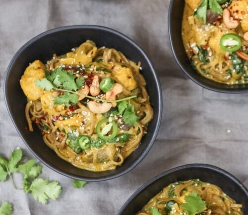Three bowls of vegan spicy coconut noodles on a table