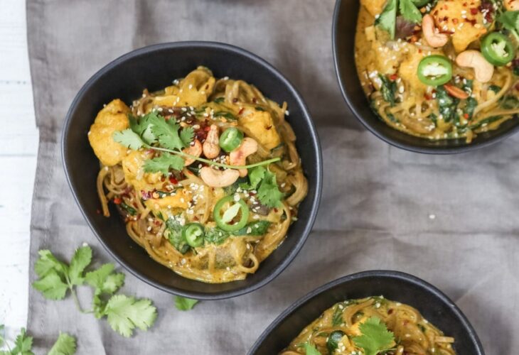 Three bowls of vegan spicy coconut noodles on a table