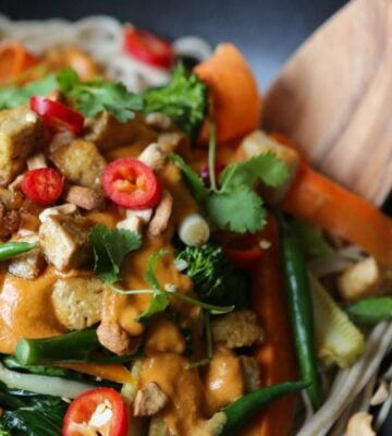 A close-up of a vegan stir fry featuring tahini, tofu, peppers, greens, carrots, and other veg