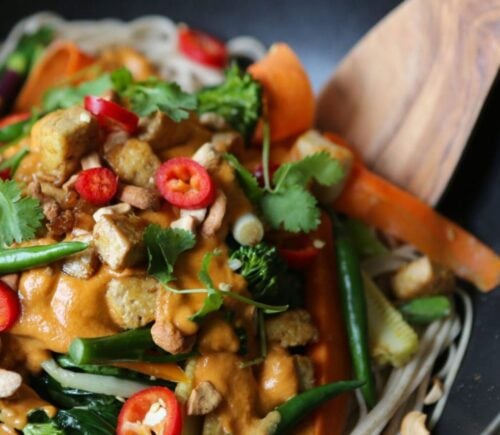 A close-up of a vegan stir fry featuring tahini, tofu, peppers, greens, carrots, and other veg