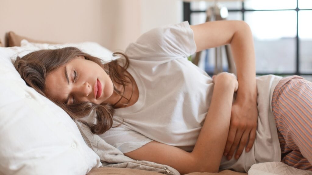 A woman lies on the bed and holds her stomach