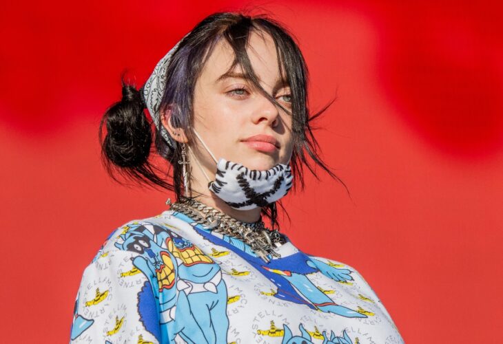 Billie Eilish on stage with a mask on her chin.