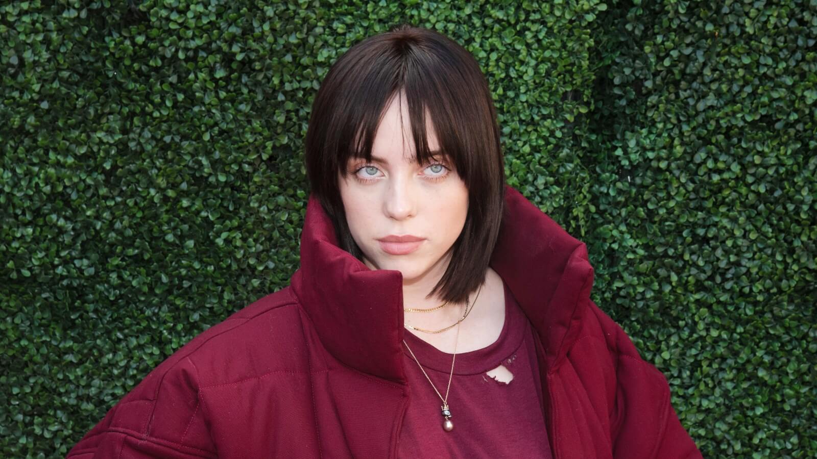 Billie Eilish standing in front of a hedge