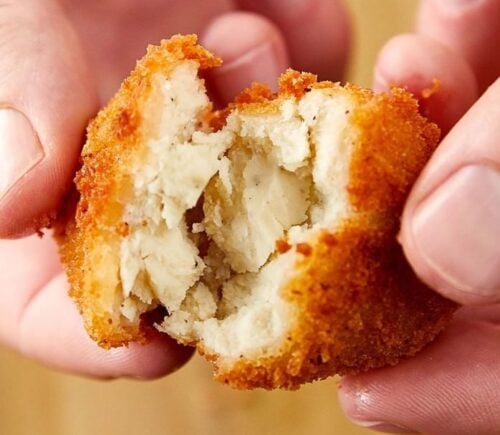 A close up of someones hands pulling apart a cultured chicken nugget