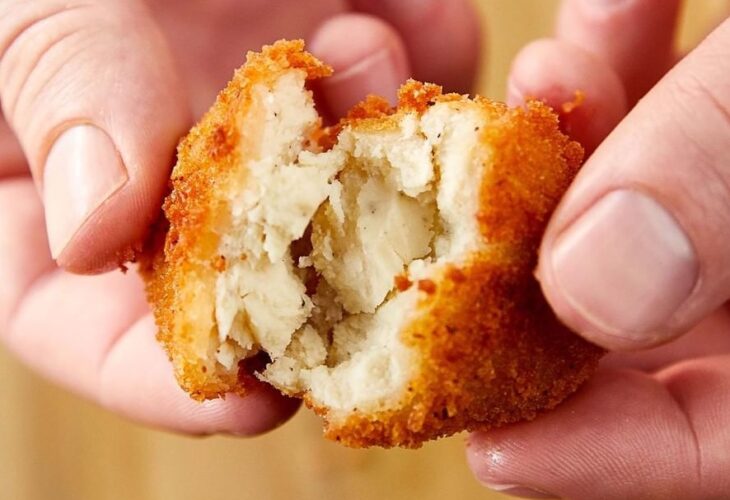 A close up of someones hands pulling apart a cultured chicken nugget