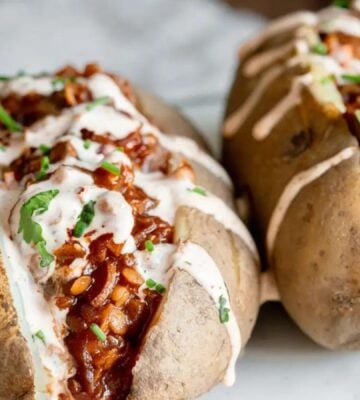 Two baked potatoes filled with smoky vegan barbecue lentils and drizzled with plant-based sriracha mayo