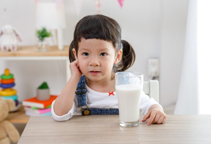 A little girl sits at a table with a glass of milk in front of her