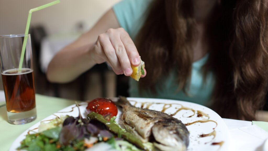 Person squeezing lemon onto a dead fish on a plate