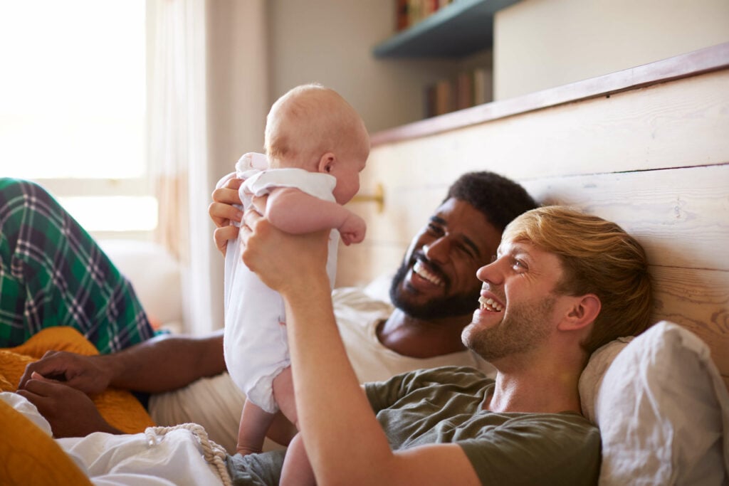 A gay couple lying in bed playing with their baby