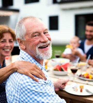 An older man sits at a table outside with his family