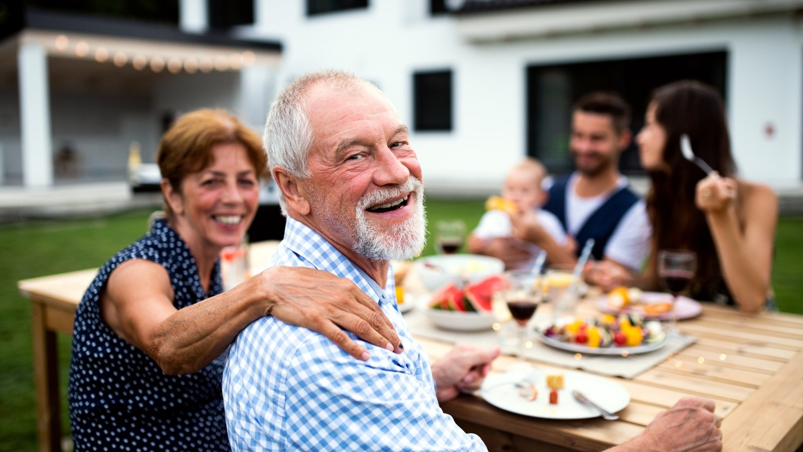 An older man sits at a table outside with his family