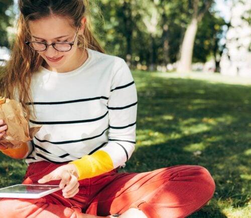 Young person sits on the grass reading and eating