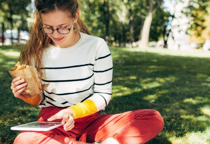 Young person sits on the grass reading and eating