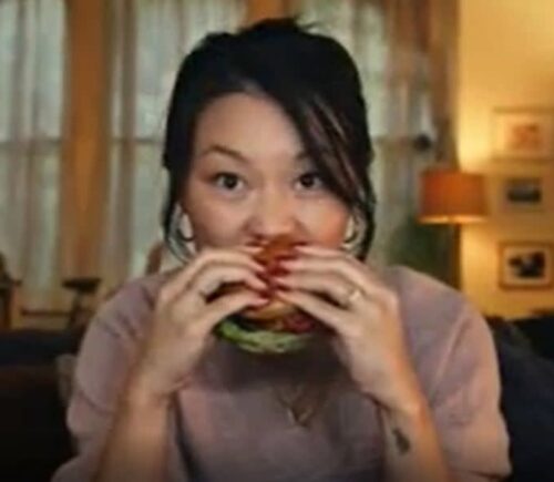 A still of Tesco's advert, a woman bites into a burger
