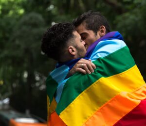 Two queer people kissing in a pride flag