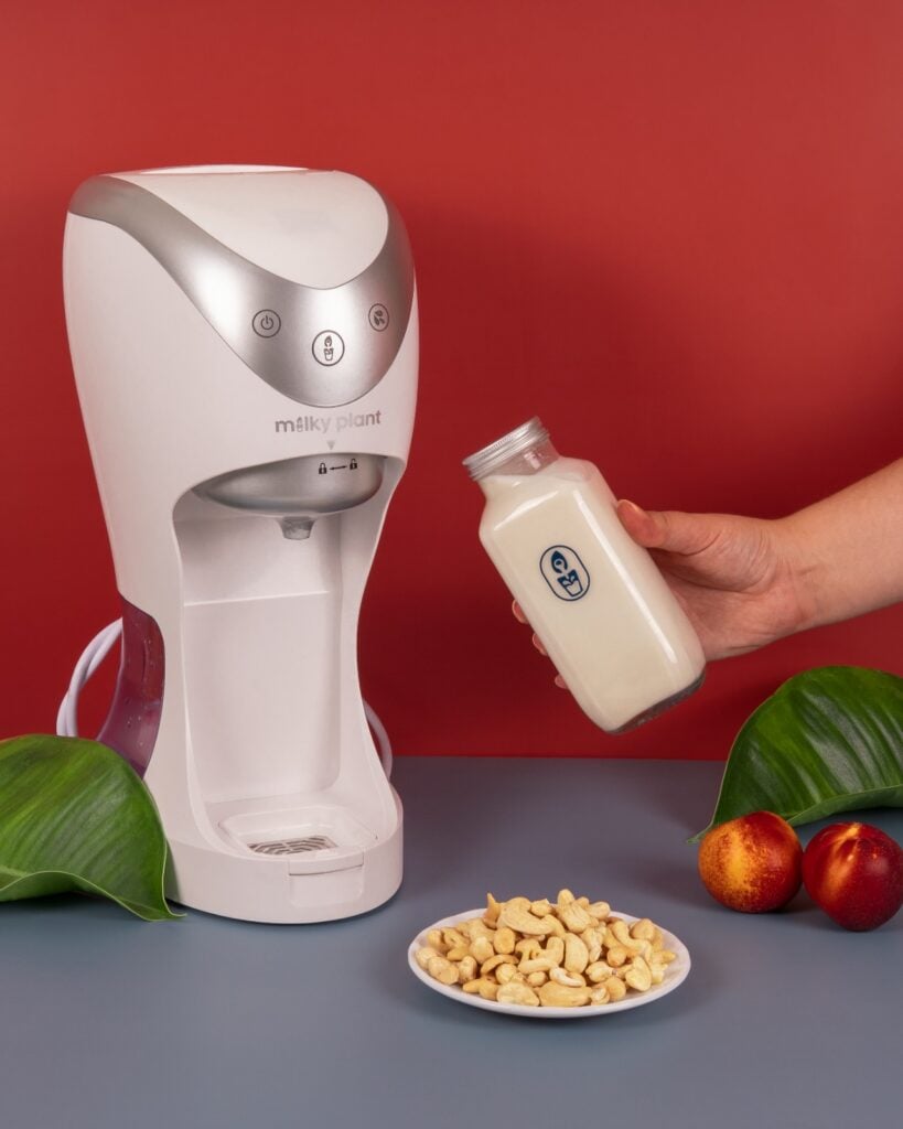 A Milky Plant appliance beside a plate of cashews and a bottle of vegan milk