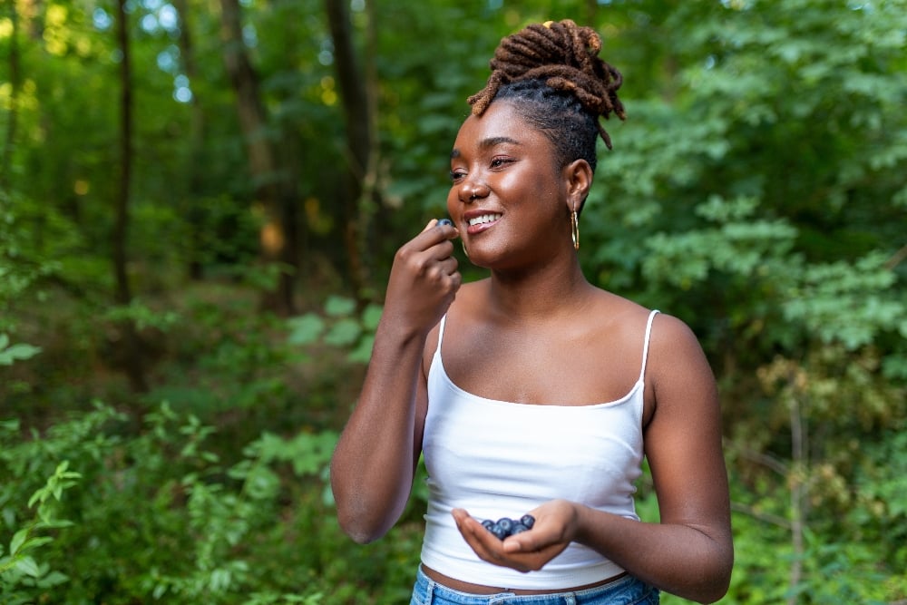 A woman eating blueberries outside surrounded by trees