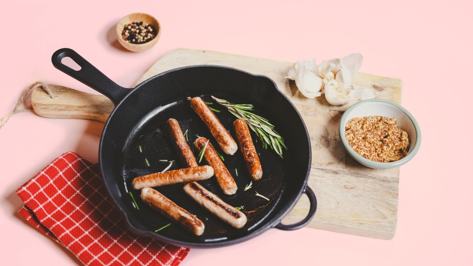 Meatable sausages in a pan against a pink background
