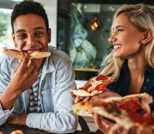 Two people eating pizza and smiling