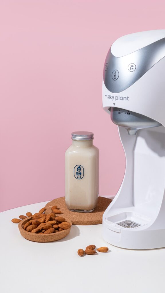 The vegan Milky Plant device beside a bottle of vegan milk and a plate of almonds