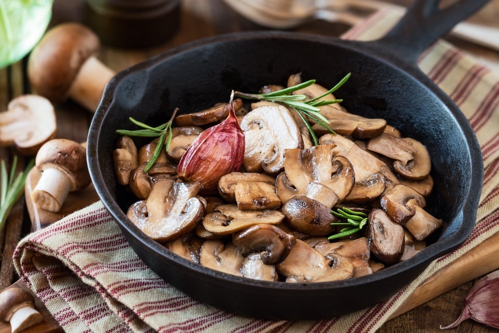 A cast iron skillet of mushrooms, a vegan source of vitamin D, with rosemary and a clove of garlic